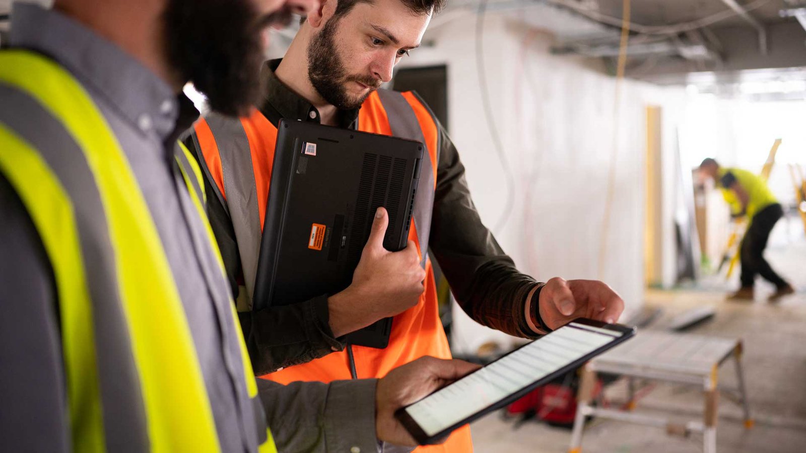 Two construction managers, standing on a building site, look at an iPad and complete a mobile form