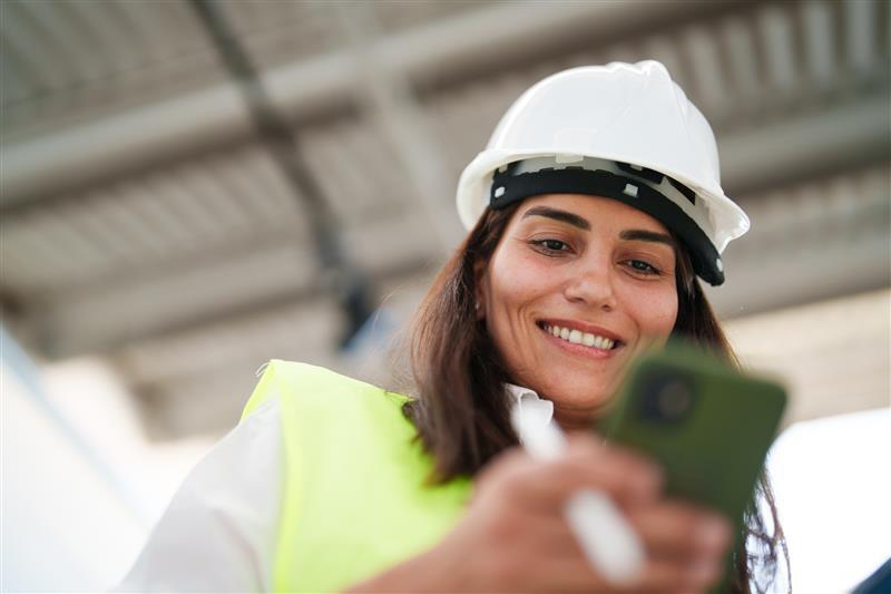 Woman wearing protective white helmet, using mobile phone at the construction site